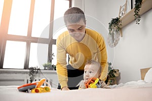 Young father does massage and useful exercises with little baby son on bed in bedroom