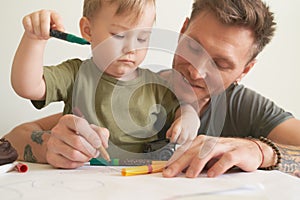 Young father helps son at age of two draw, teaches
