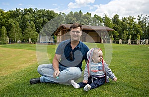 Young father with his 9 months old baby boy relaxing on grass at