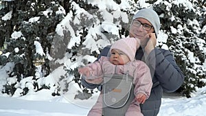 Young father with his baby in carrier with phone talking working father