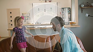 A young father and his cute happy little daughter having pillow fight on the sofa. Slow motion, Steadicam shot