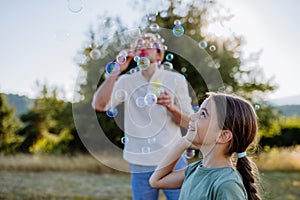 Young father and his little daughter having fun while blowing soap bubbles on a summer day in nature.