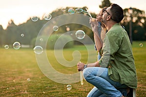 Young father and his little girl having fun while blowing soap bubbles on a summer day, daughter and dad spending time