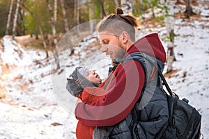 Young father and his little son in an ergonomic sling walk through the forest and look at each other