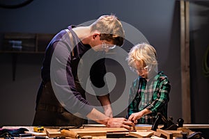 a young father and his little son make a toy out of wood in a carpenter's workshop.