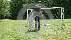 Young father with his little son playing football on football pitch