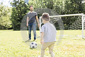 Young father with his little son playing football on football pitch