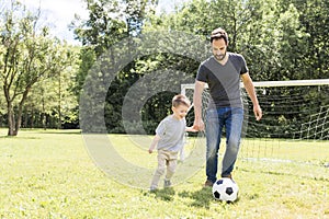 Young father with his little son playing football on football pitch