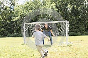 Young father with his little son playing football on football pitch