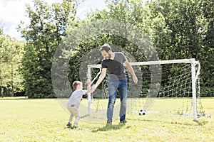 Young father with his little son playing football on football pitch