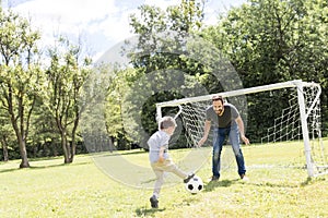 Young father with his little son playing football on football pitch