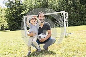 Young father with his little son playing football on football pitch