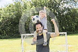 Young father with his little son playing football on football pitch