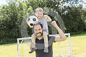 Young father with his little son playing football on football pitch