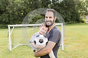 Young father with his little son playing football on football pitch