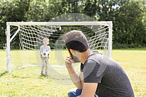 Young father with his little son playing football on football pitch