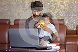 Young father with his little son working on laptop at home - Concept of work form home or wfh reality, People Lifestyles