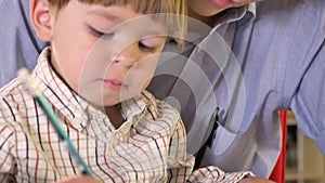 Young father and his little son writing on paper and holding tablet, dad helping and teaching his son how to write