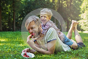Young father and his son eating strawberries in Park. Picnic. Outdoor portrait