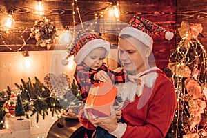 Young father and his son in Santa`s hat open a Christmas gift present box. Winter holidays and childhood concept