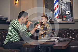 Young father and his stylish little son in the barbershop in the waiting room.