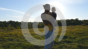 Young father holds on hands his son in the meadow at nature at sunny summer day. Dad and little boy hugging outdoor and