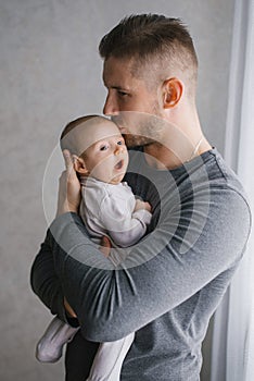 A young father holds his little son in his arms and kisses him, the baby yawns