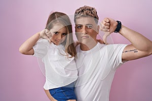 Young father hugging daughter over pink background with angry face, negative sign showing dislike with thumbs down, rejection