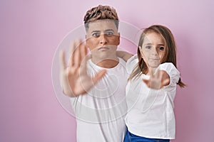 Young father hugging daughter over pink background with open hand doing stop sign with serious and confident expression, defense