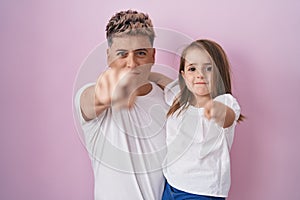 Young father hugging daughter over pink background pointing with finger to the camera and to you, confident gesture looking