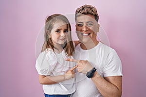 Young father hugging daughter over pink background smiling happy pointing with hand and finger