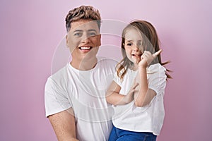 Young father hugging daughter over pink background smiling happy pointing with hand and finger to the side