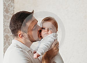 Young father kisses baby daughter in a light room close-up