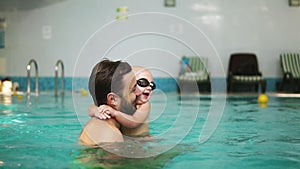 Young father lifting his little boy in protective glasses from the water while teaching him how to swim in the swimming