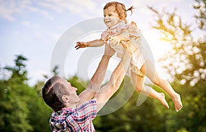 Young father lifting up her toddler laughing little daughter overhead in the air - Dad and his baby playing together outdoors in