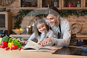 Young Father And Little Daughter Preparing Meal In Kitchen Together, Checking Recipe
