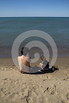 Young father and little daughter sitting on the beach and playing with sand