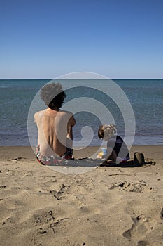Young father and little daughter sitting on the beach and playing with sand