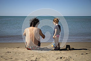 Young father and little daughter sitting on the beach and playing with sand