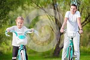 Young father and little girl biking at summer warm day. Young active family ride on bicycles