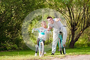 Young father and little girl biking at summer warm day. Young active family ride on bicycles