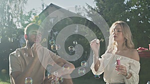 Young father and mother makes a bubble of soap bubbles outdoors