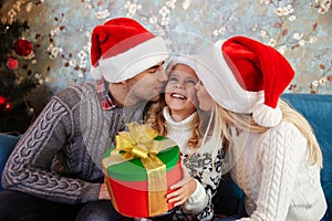 Young father and mother in Santa`s hat kissing those little daug