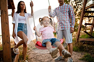 Young father and mother swing their cute little daughter on swing