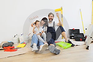 Young father mother and their little girl daughter with wall paint rollers sitting on the floor