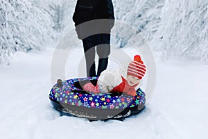 Young father pull little toddler girl on snow tube. Cute little happy child having fun outdoors in winter on colorful