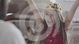 Young father putting the crown on the head of his little daughter, making her princess close up. The girl is happy, she