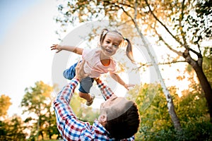 Young father raises his cheerful daughter high up with his hands