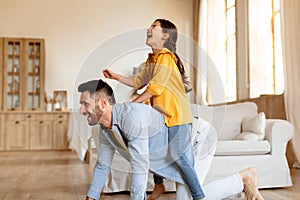 Young father riding daughter on back fooling at home