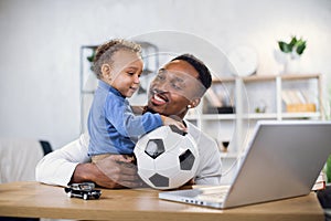 Young father and son playing with ball and using laptop